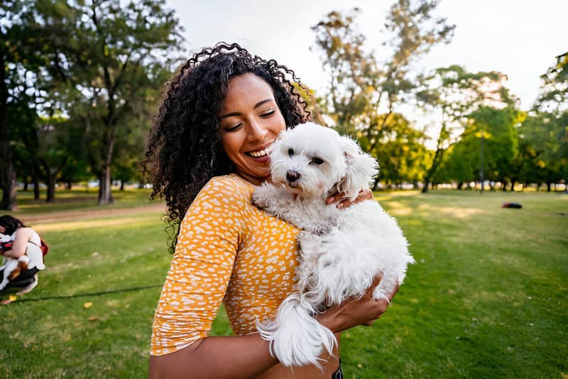 Mujer sonriente con su mascota en brazos en medio de un parque
