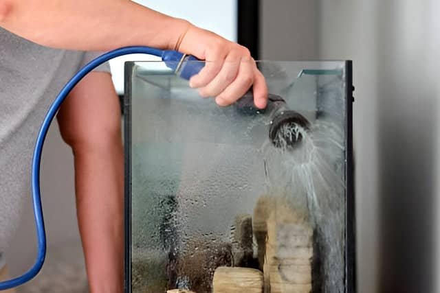 Hombre limpiando un acuario de peces de agua dulce con cuidado, utilizando herramientas para mantener el agua limpia y saludable.